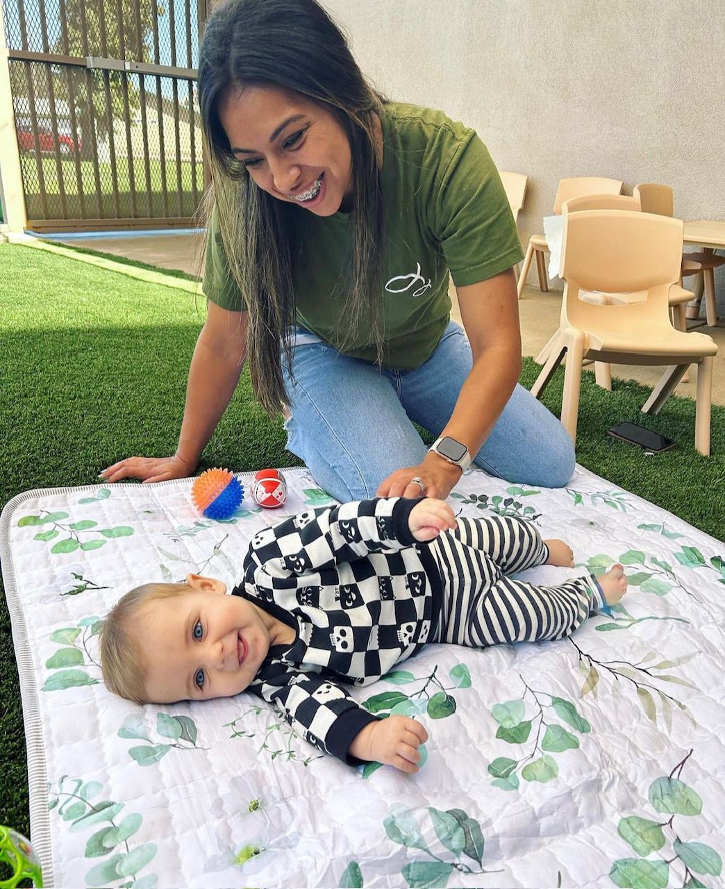 A woman is playing with a baby on a blanket.