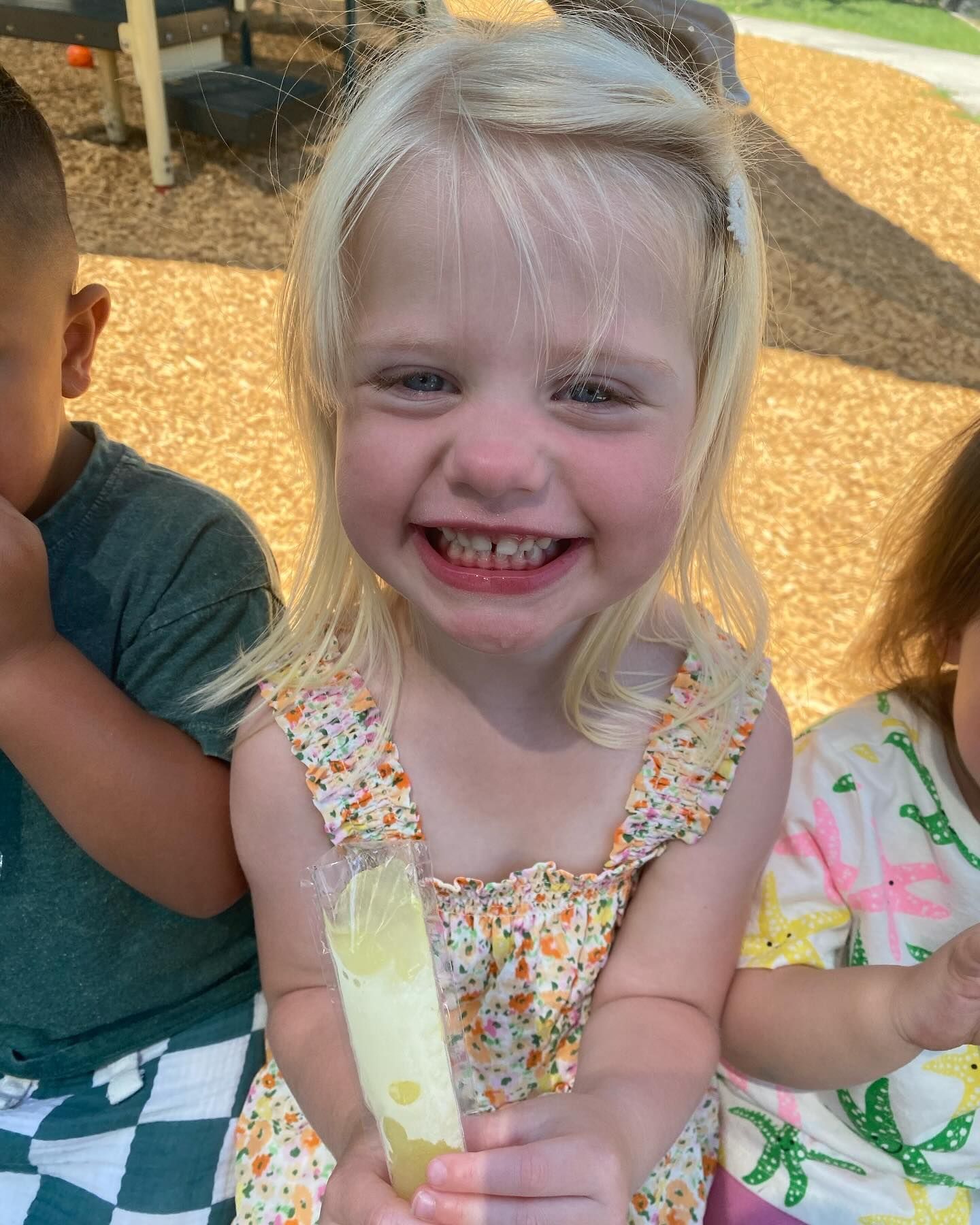 A little girl is holding a popsicle in her hand and smiling.