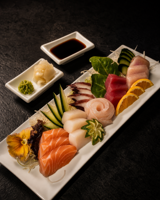 Assorted sushi and sashimi on a white platter with soy sauce and condiments on a dark table