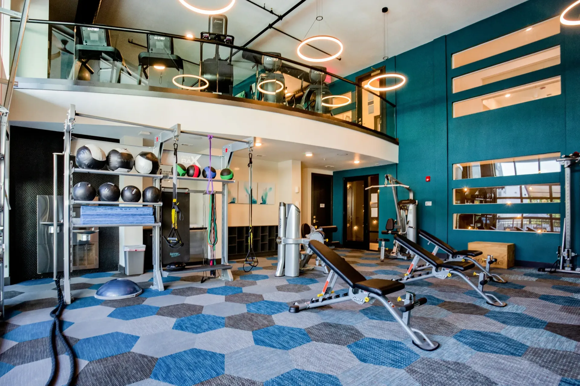 Modern apartment gym with cardio and strength equipment, teal walls, and circular ceiling lights.