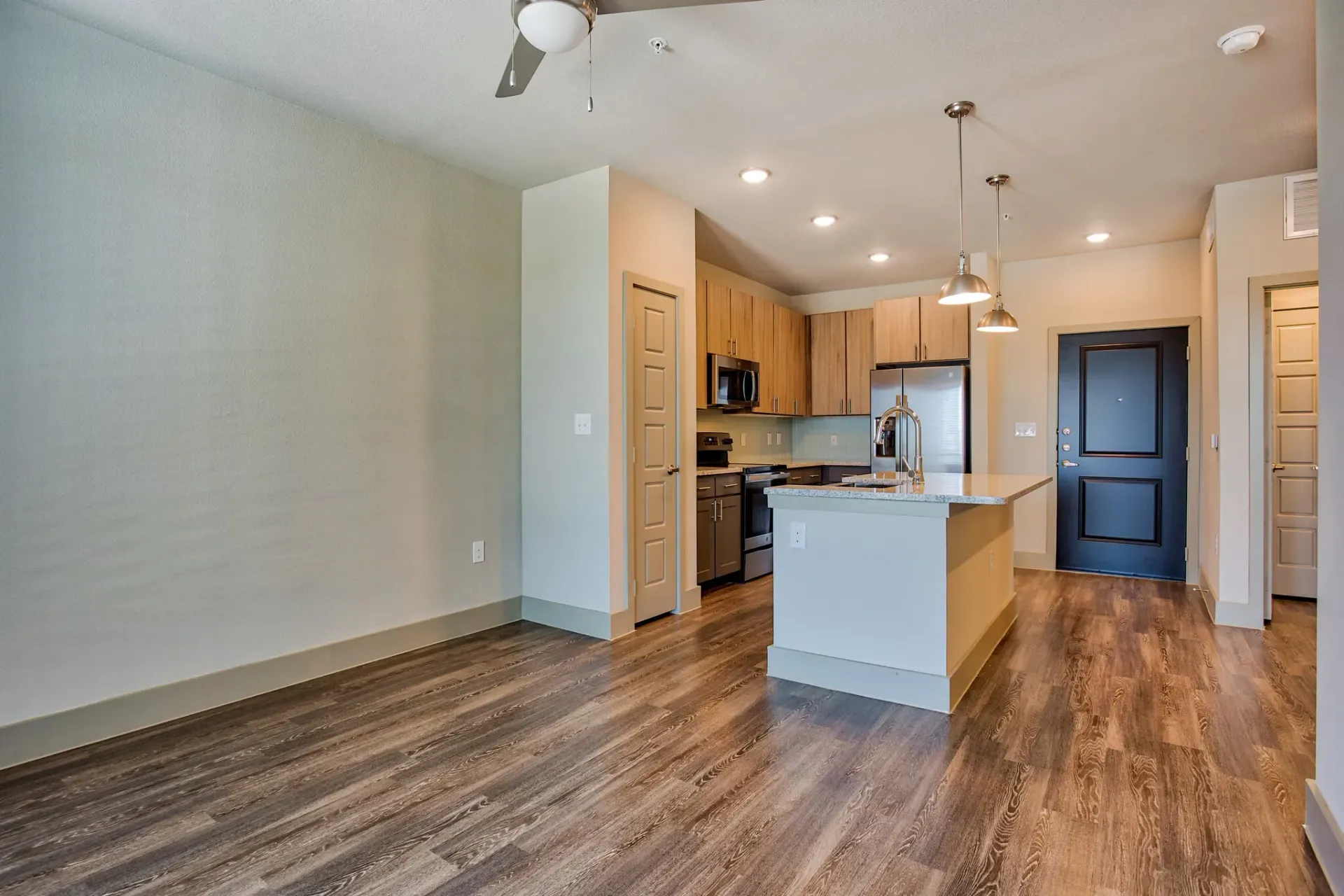 Open-concept living area with kitchen island, stainless-steel appliances, and wood-style flooring.
