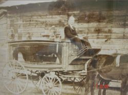Person riding in a horse-drawn carriage beside a stone wall, sepia-toned historic photo