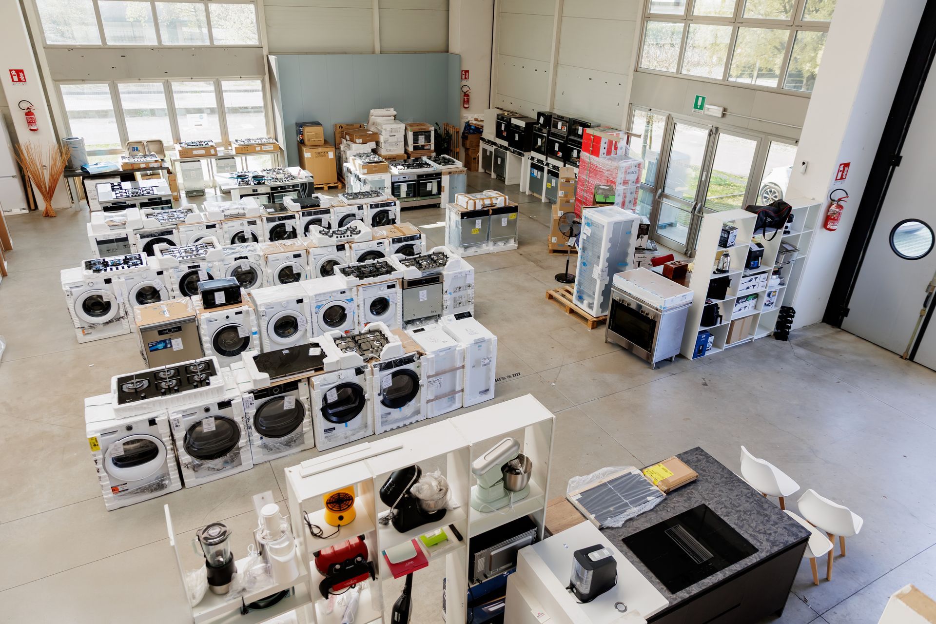 Uno showroom a cielo aperto, in stile magazzino, che espone file di lavatrici e altri elettrodomestici su un pavimento di cemento.