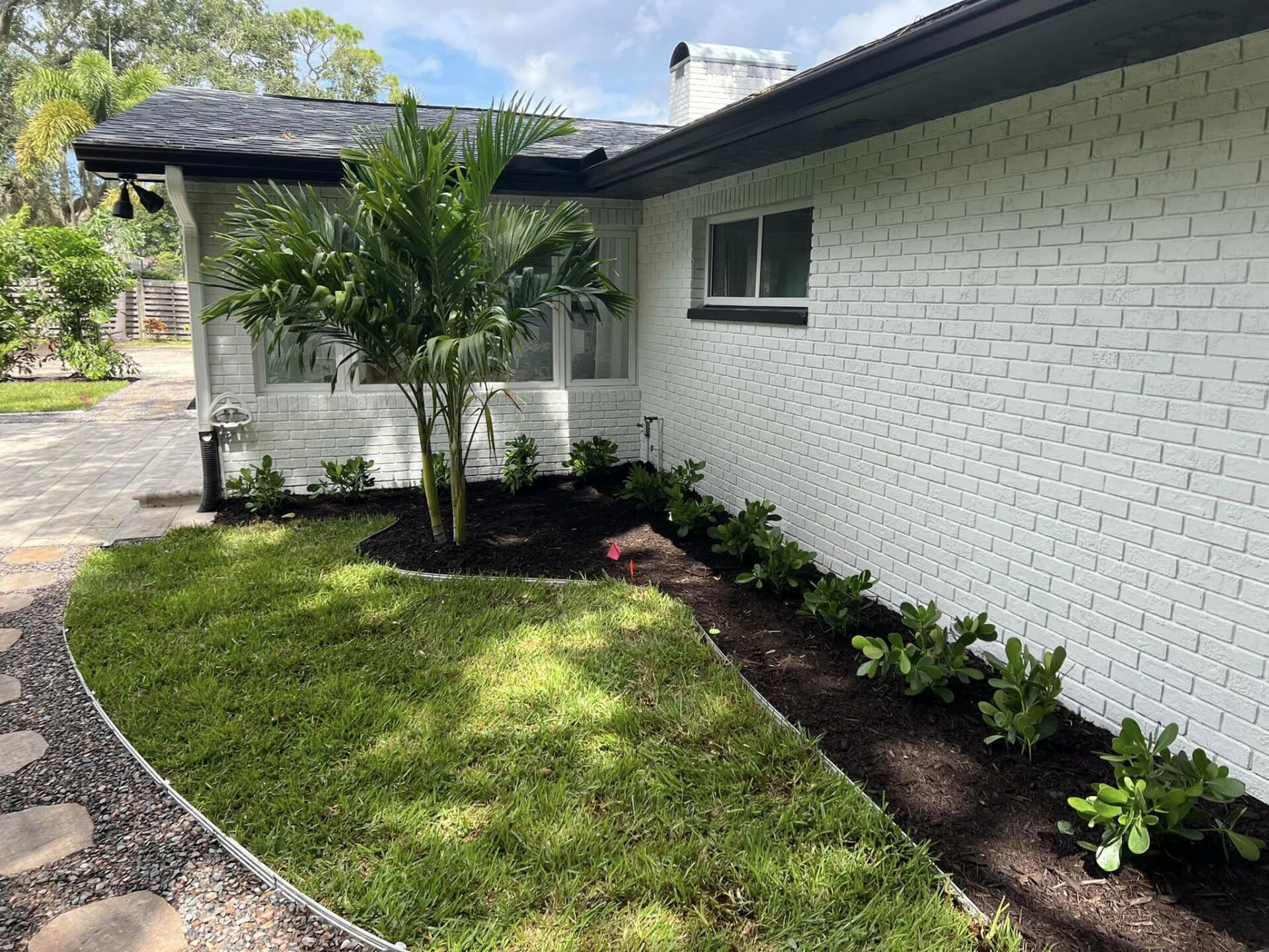 White brick house with new landscaping, including green grass, mulch, and plants.