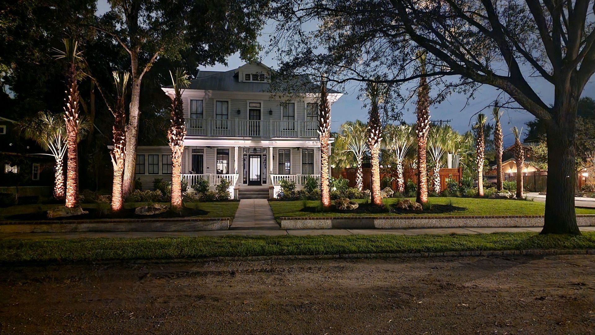 Lit up white Victorian house at night, with palm trees along the front yard.