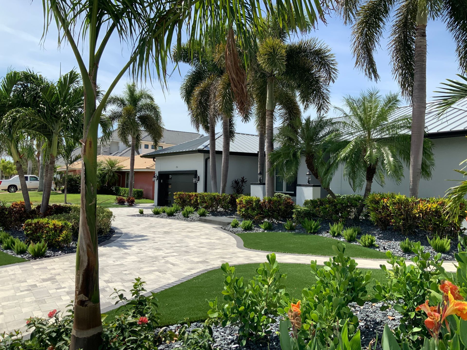 A driveway leading to a house surrounded by palm trees and flowers.