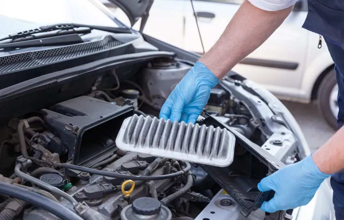 Mechanic in blue gloves replacing car air filter in engine bay.