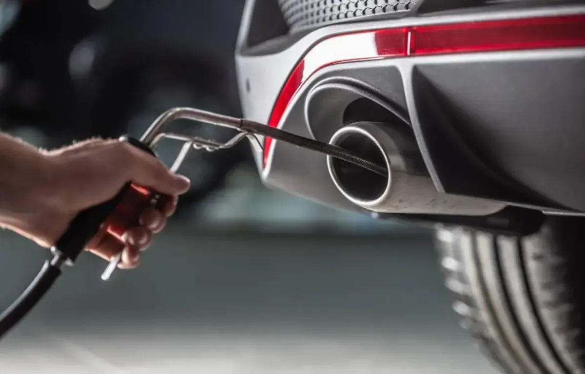Hand holding exhaust emission tester inserted into a car's tailpipe.