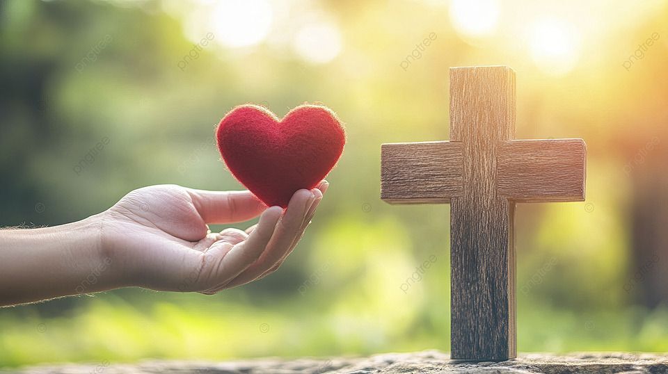 A person is holding a red heart in front of a wooden cross.