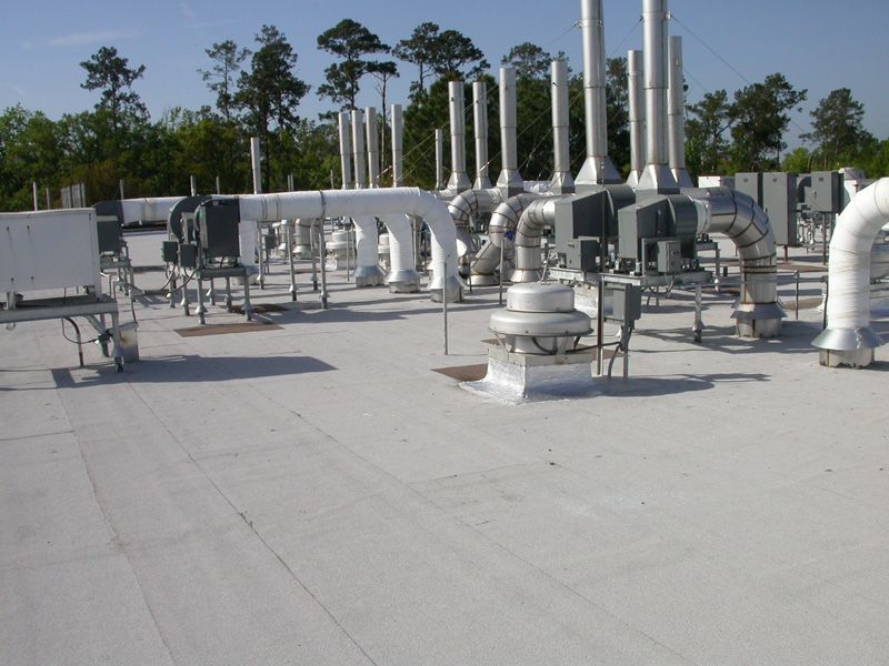Rooftop view of commercial HVAC equipment with metal exhaust stacks on a flat, light-colored roof.
