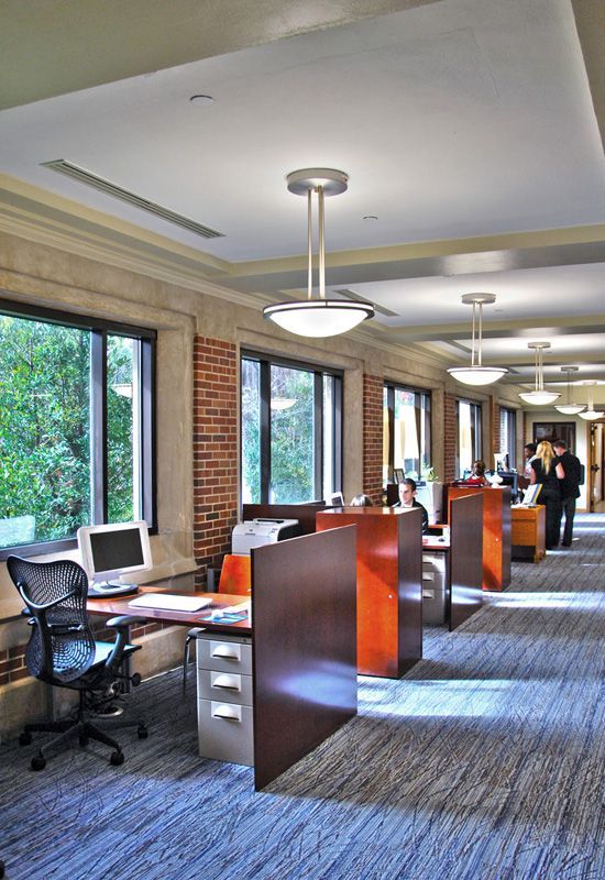 Office space with rows of desks, windows, and overhead lights.