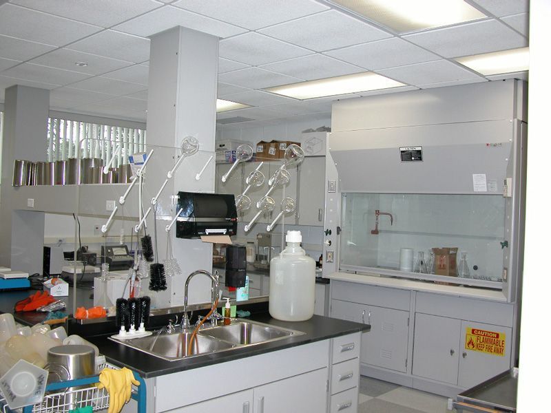 Laboratory interior with lab equipment, sink, and fume hood. Gray and white colors dominate.