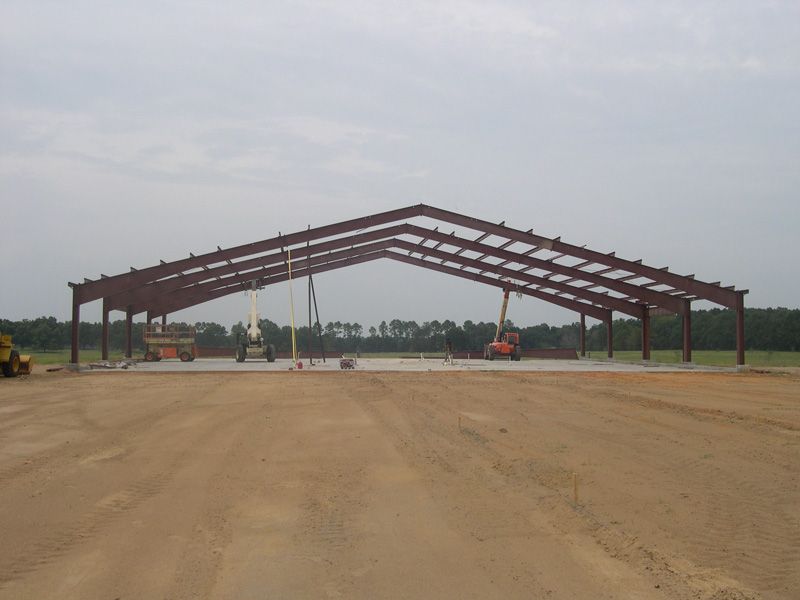 Steel frame of a building under construction on a dirt lot; orange construction equipment visible.
