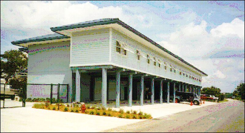 Light blue building on stilts with a dark roof and a paved driveway.