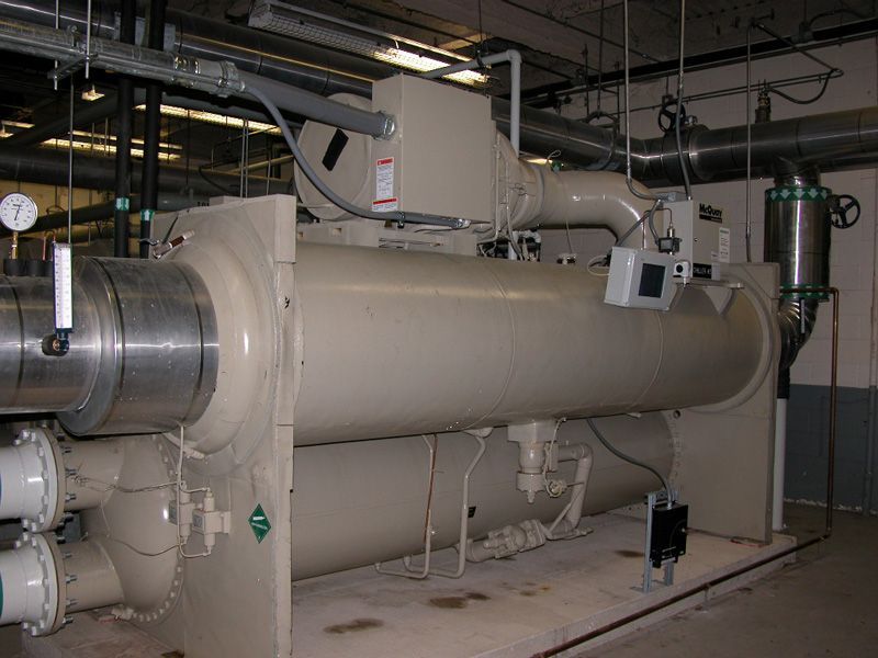 Large, beige industrial chiller in a mechanical room, with pipes and gauges visible.