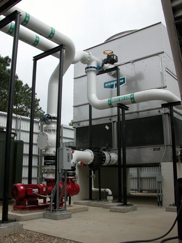 Cooling tower system with white pipes and red pump, outdoors.