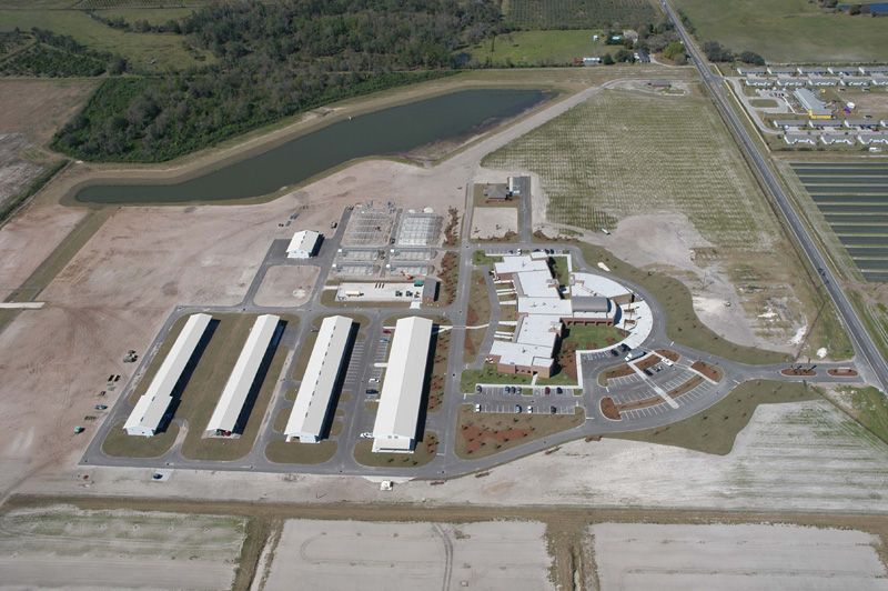 Aerial view of a large facility with multiple buildings, a pond, and surrounding fields.