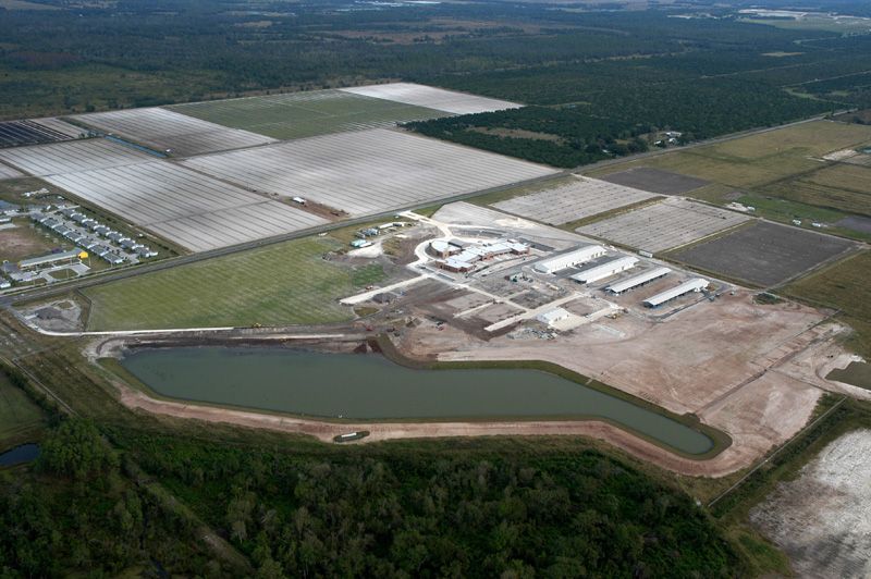 Aerial view of a large agricultural complex with greenhouses, barns, a water reservoir, and surrounding fields.