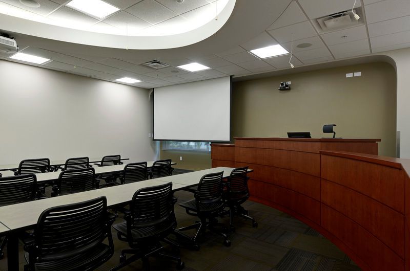 Classroom with rows of chairs and tables, a projection screen, and a wooden podium.