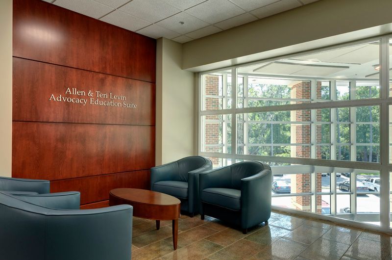 Waiting area with blue chairs, small table, wooden wall, and large windows.