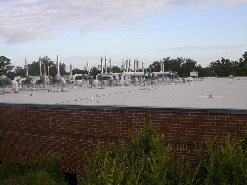 White pipes on a flat roof of a brick building, with trees in the background under a cloudy sky.