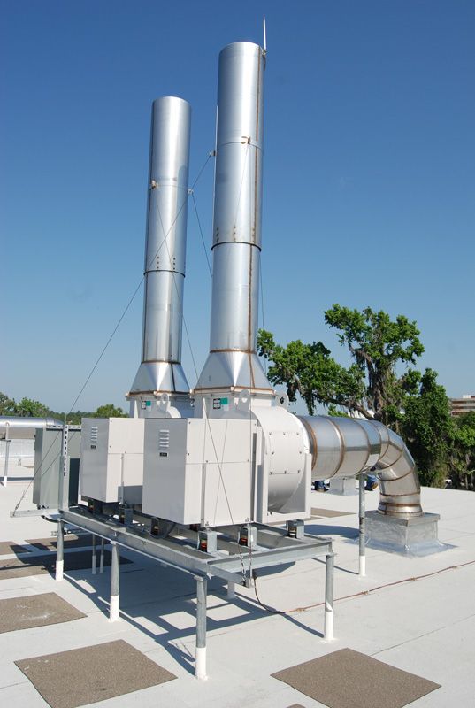 Two large metal exhaust stacks on a building rooftop against a blue sky.