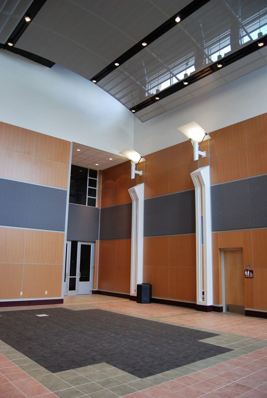 Interior view of a modern building lobby with tan, gray, and white walls. Floor has a dark mat.
