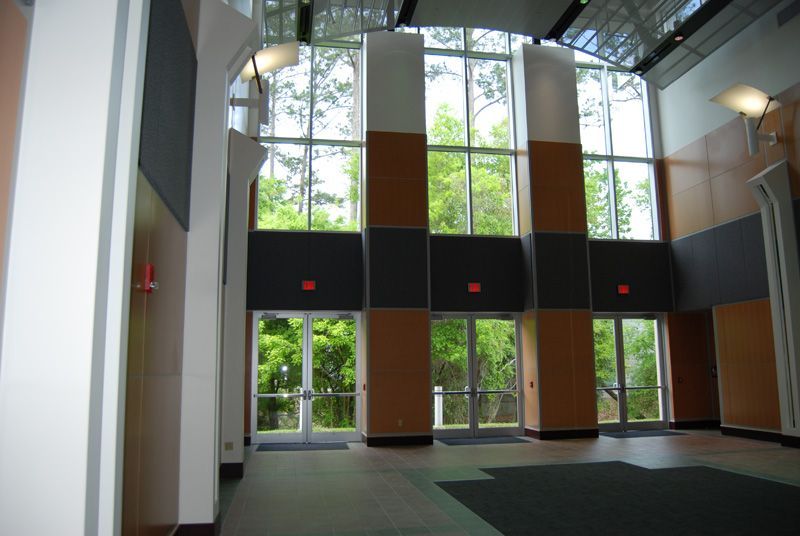 Interior lobby with tall windows overlooking trees and multiple exit doors. Beige, brown, and gray walls.