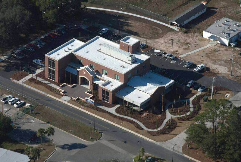 Aerial view of a brick building with a flat roof, surrounded by a parking lot and landscaping.