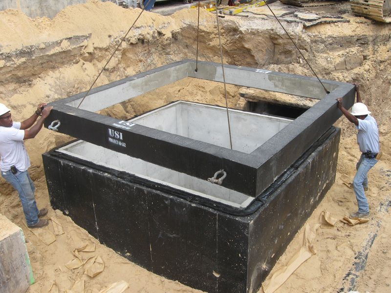 Two workers installing a concrete manhole frame in a construction site.