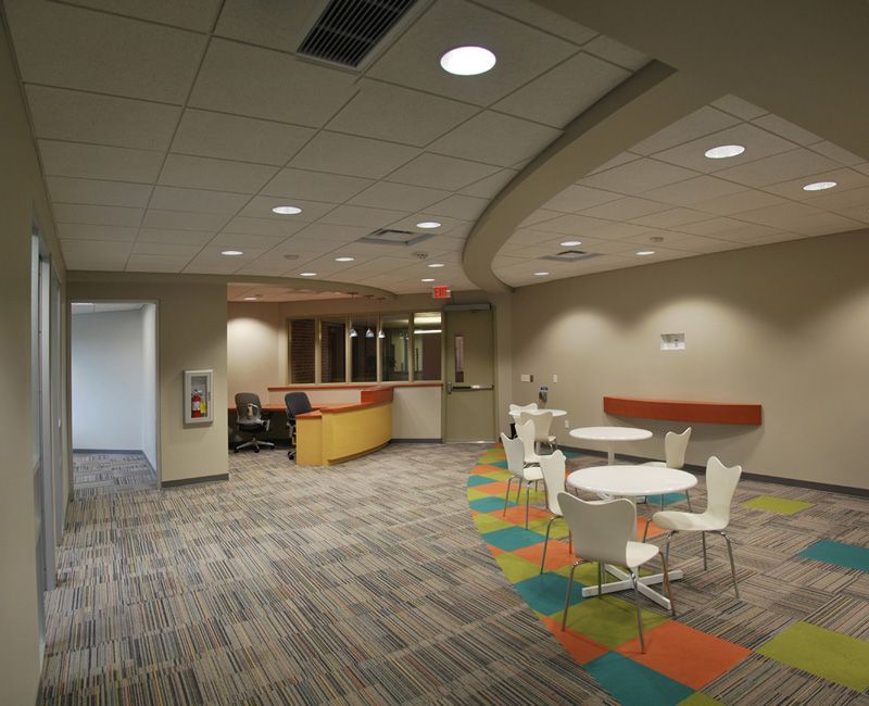 Reception area with curved ceiling, tables, chairs, and colorful carpet.