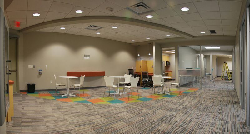 Empty waiting area with tables, chairs, colorful floor tiles, and a hallway.