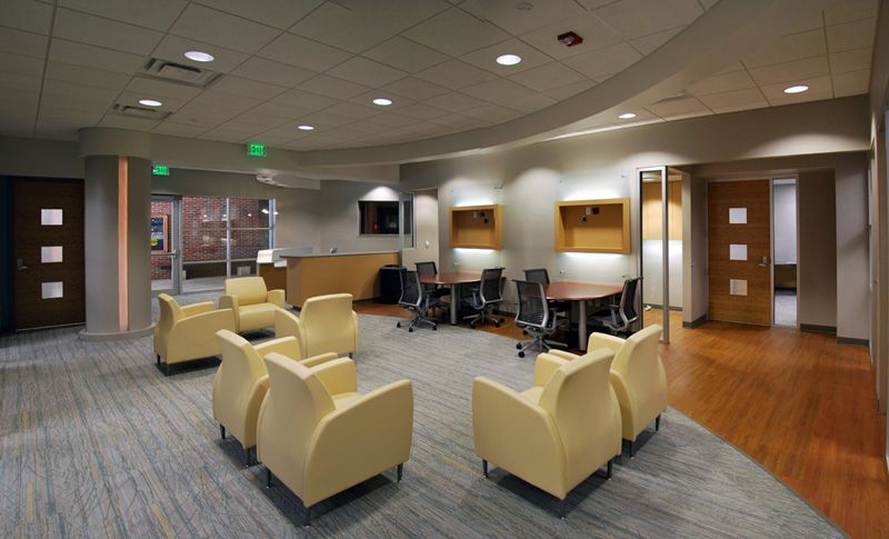 Lounge with cream armchairs on patterned rug, meeting room with round table and chairs, and hallway with wooden floors.