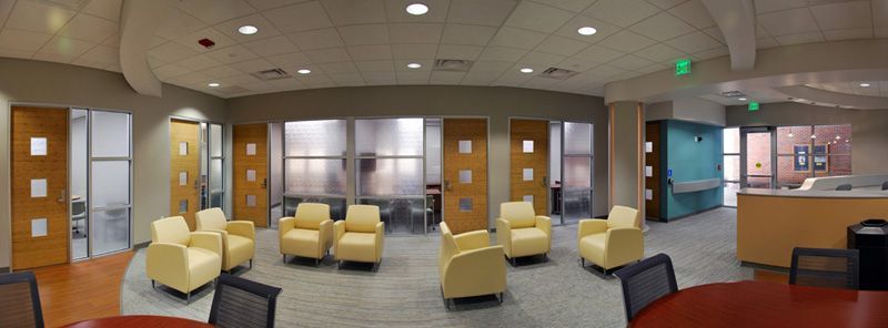 A modern waiting area with light yellow armchairs, wooden doors, and large windows.