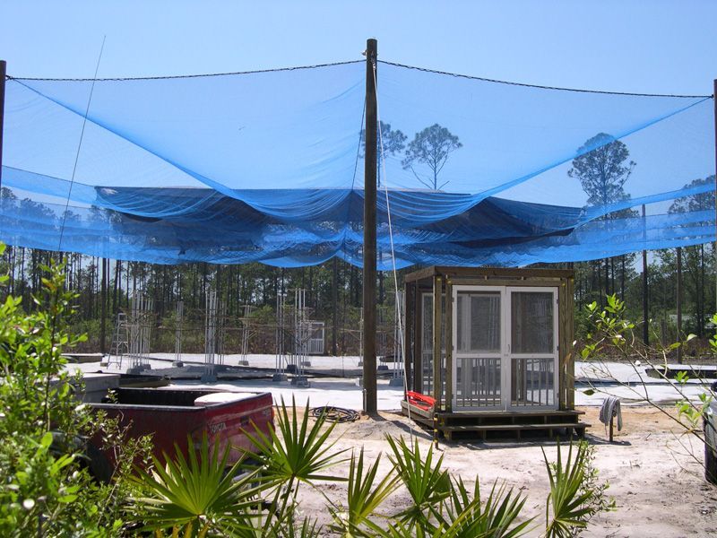 Blue netting canopy over a wooden structure and concrete foundation.  Outdoor setting with trees in the background.