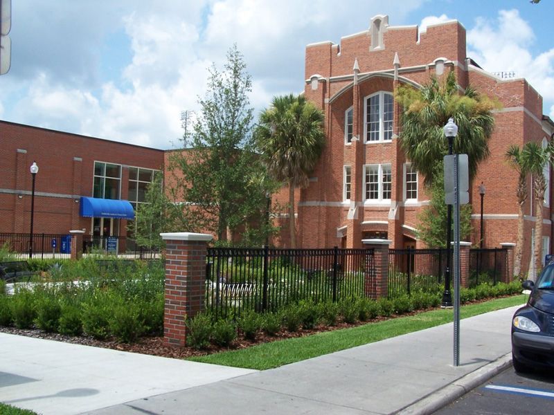 Brick building with arched windows, blue awning, black fence, and palm trees.