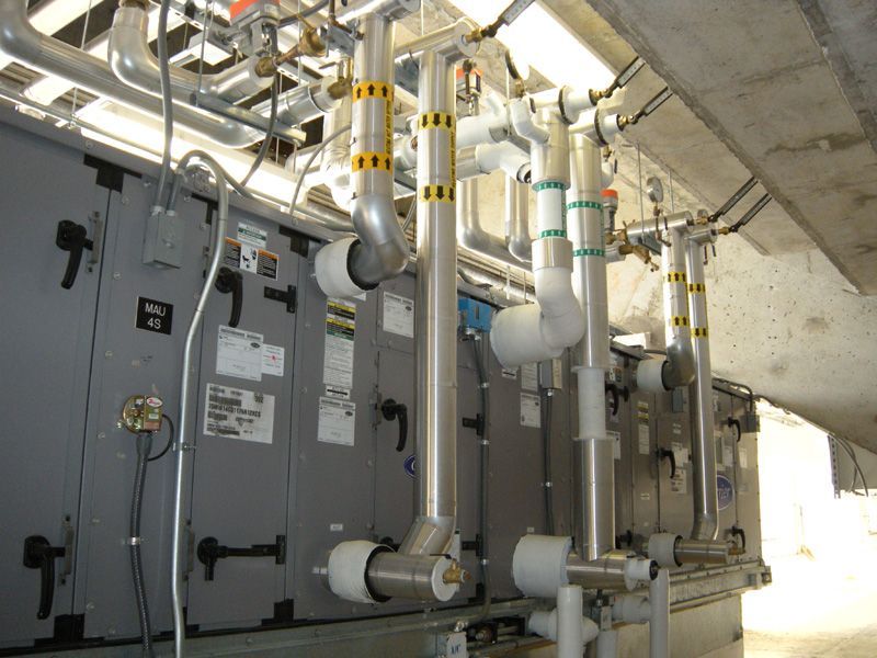 Industrial HVAC units with insulated pipes, under a concrete overhang.