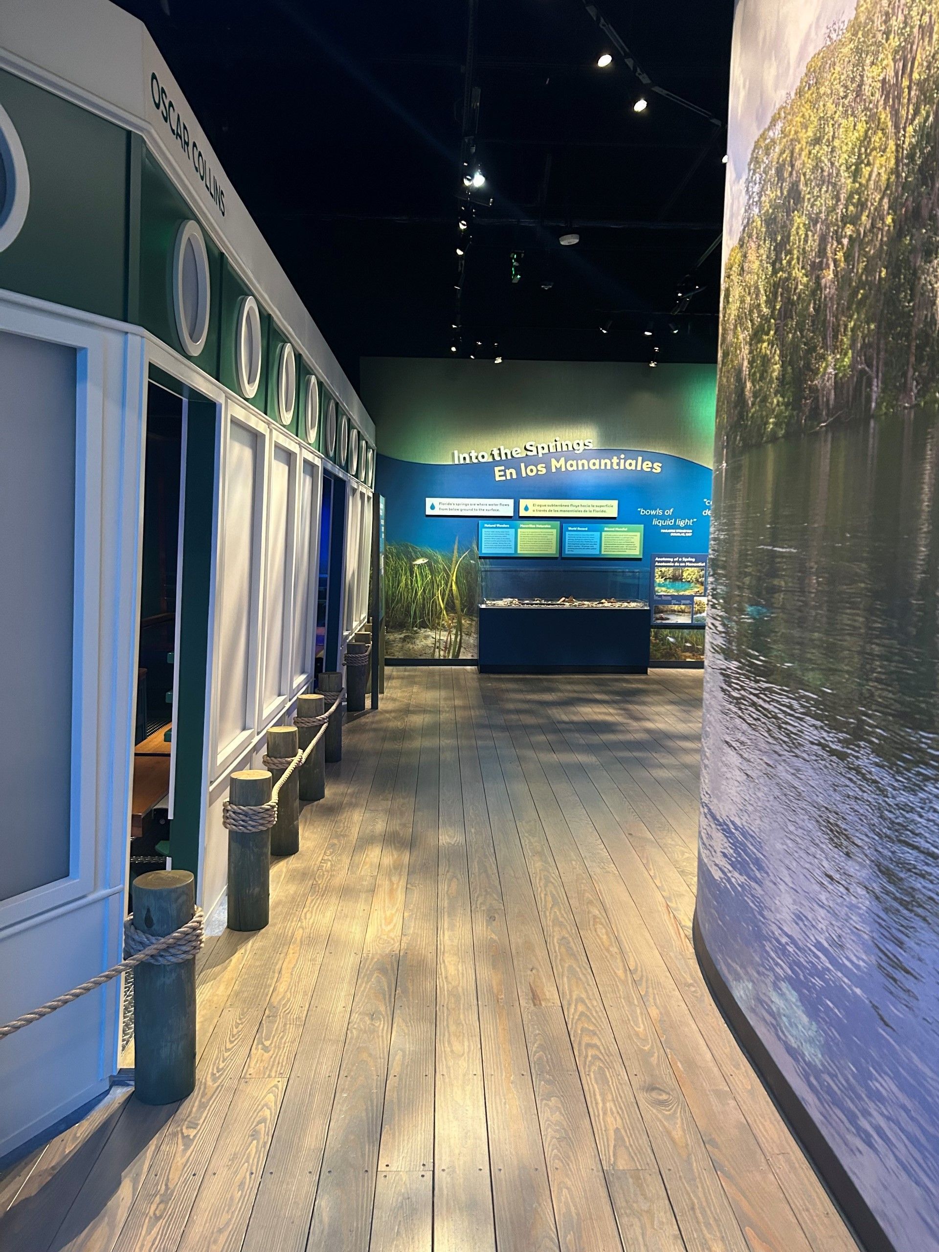 Museum exhibit: hallway with green walls, porthole windows, wood floor, and water-themed mural.