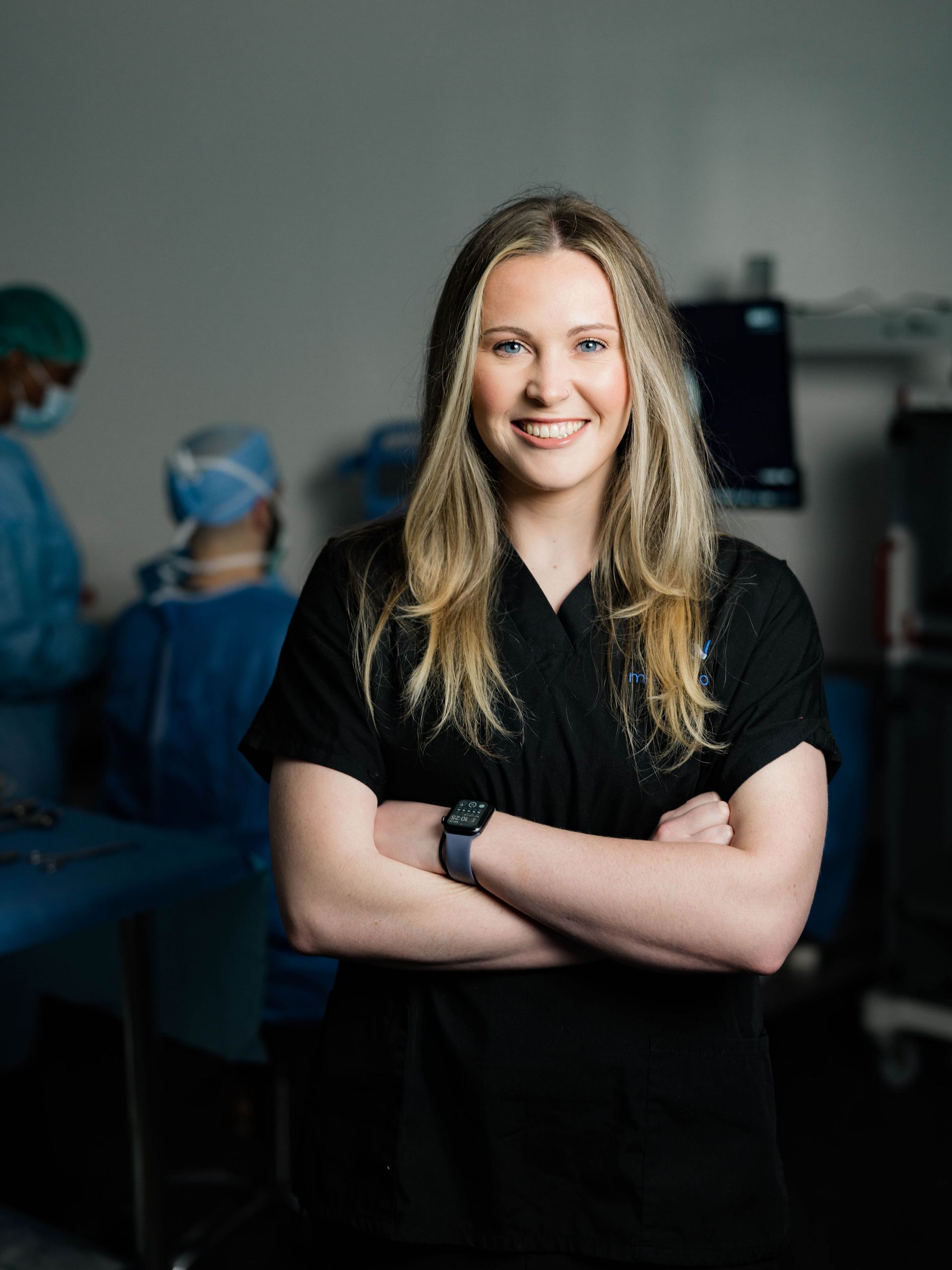 A woman is standing in an operating room with her arms crossed and smiling.