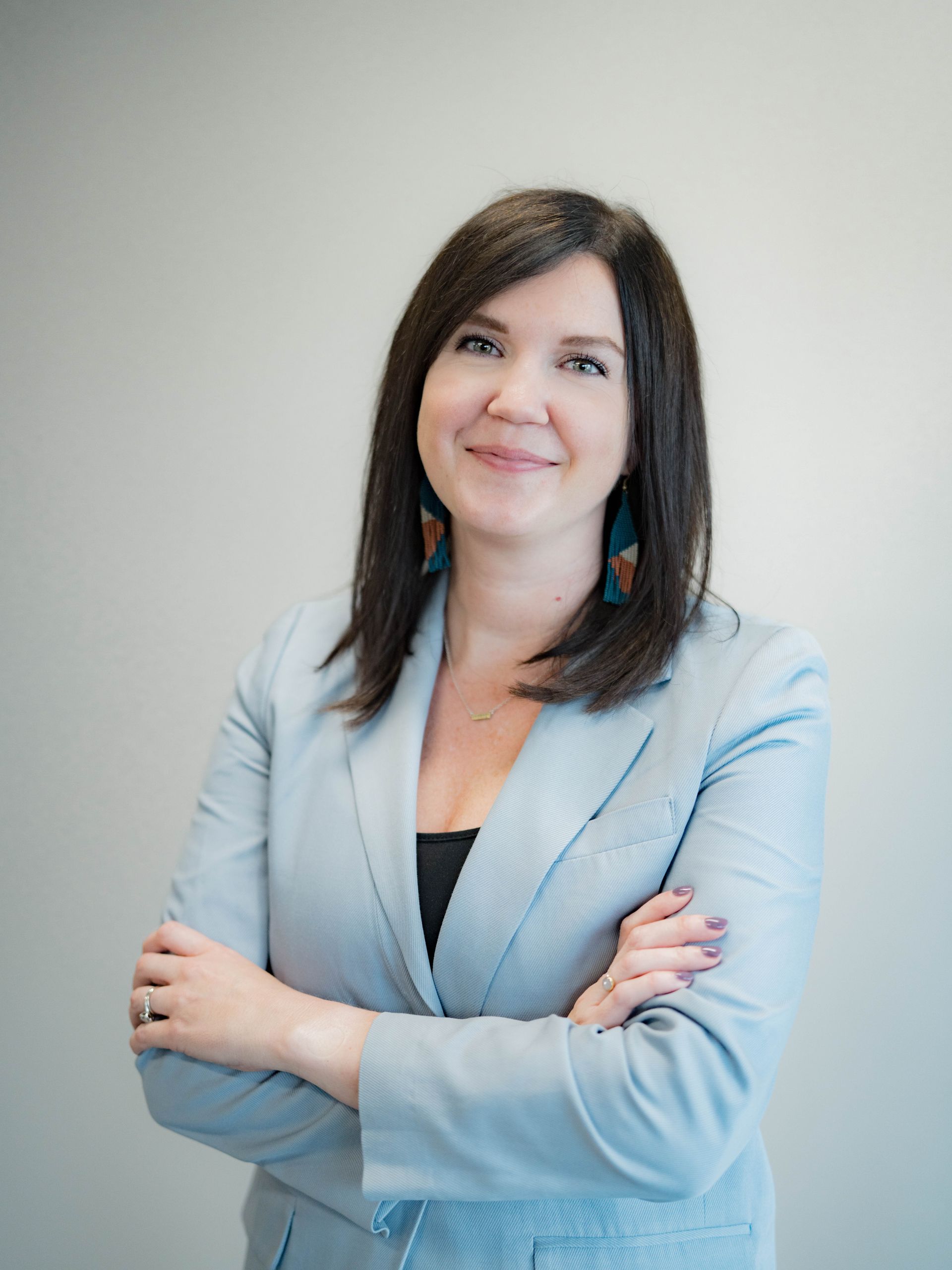 A woman in a suit is standing with her arms crossed and smiling.