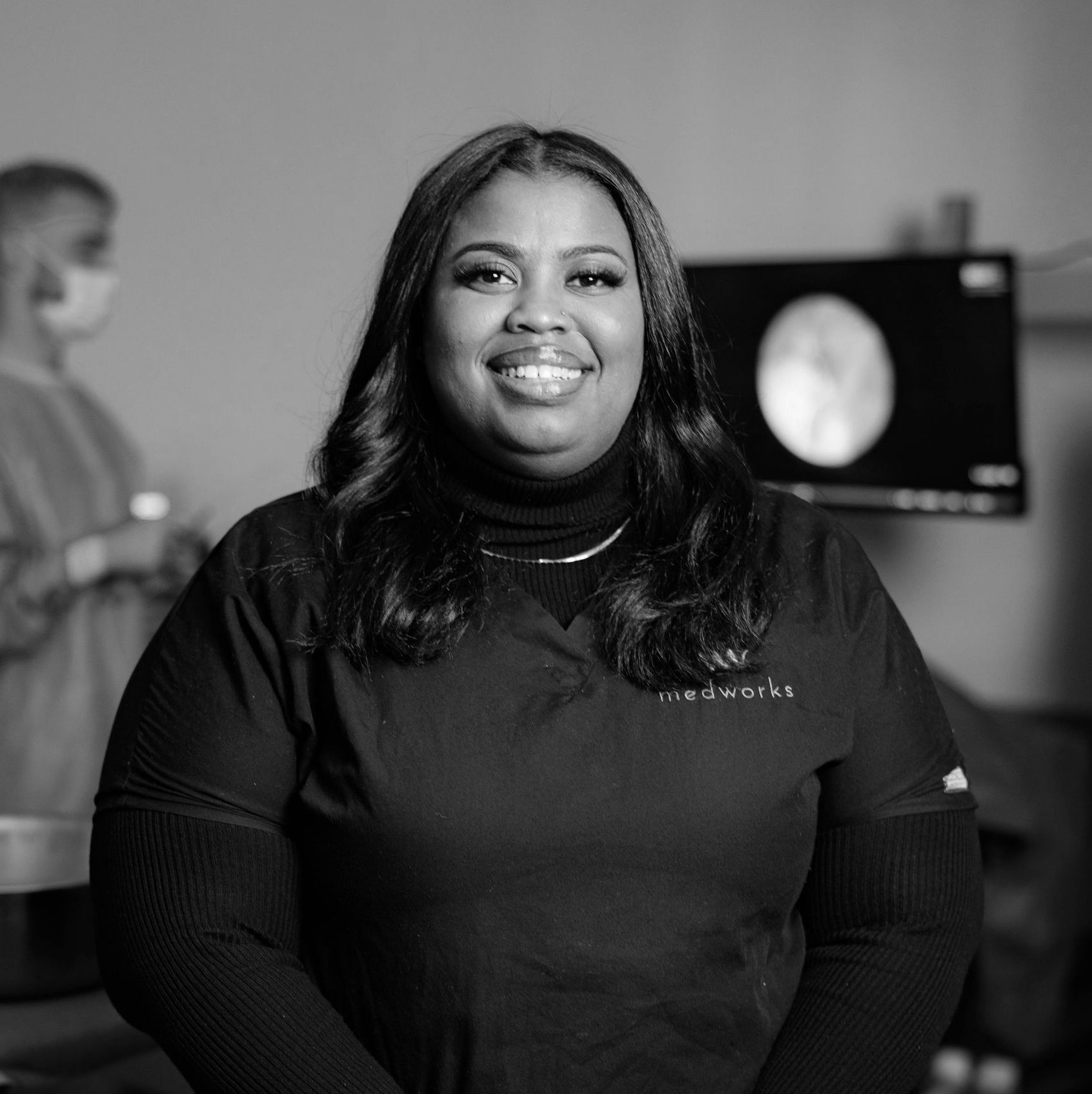 A black and white photo of a smiling woman in a scrub top.