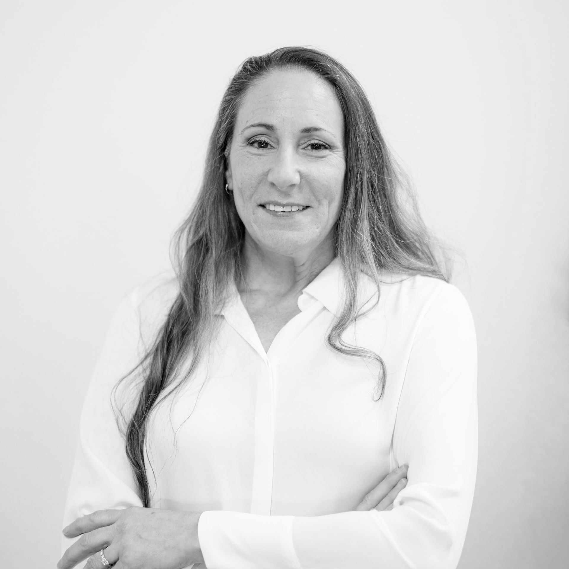Woman in a white blouse standing with arms crossed against a plain light background