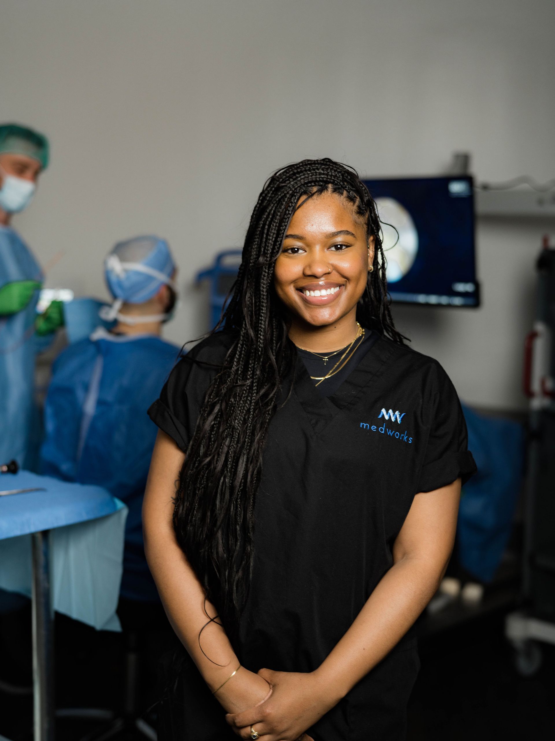 A woman in a black scrub top is smiling in an operating room.