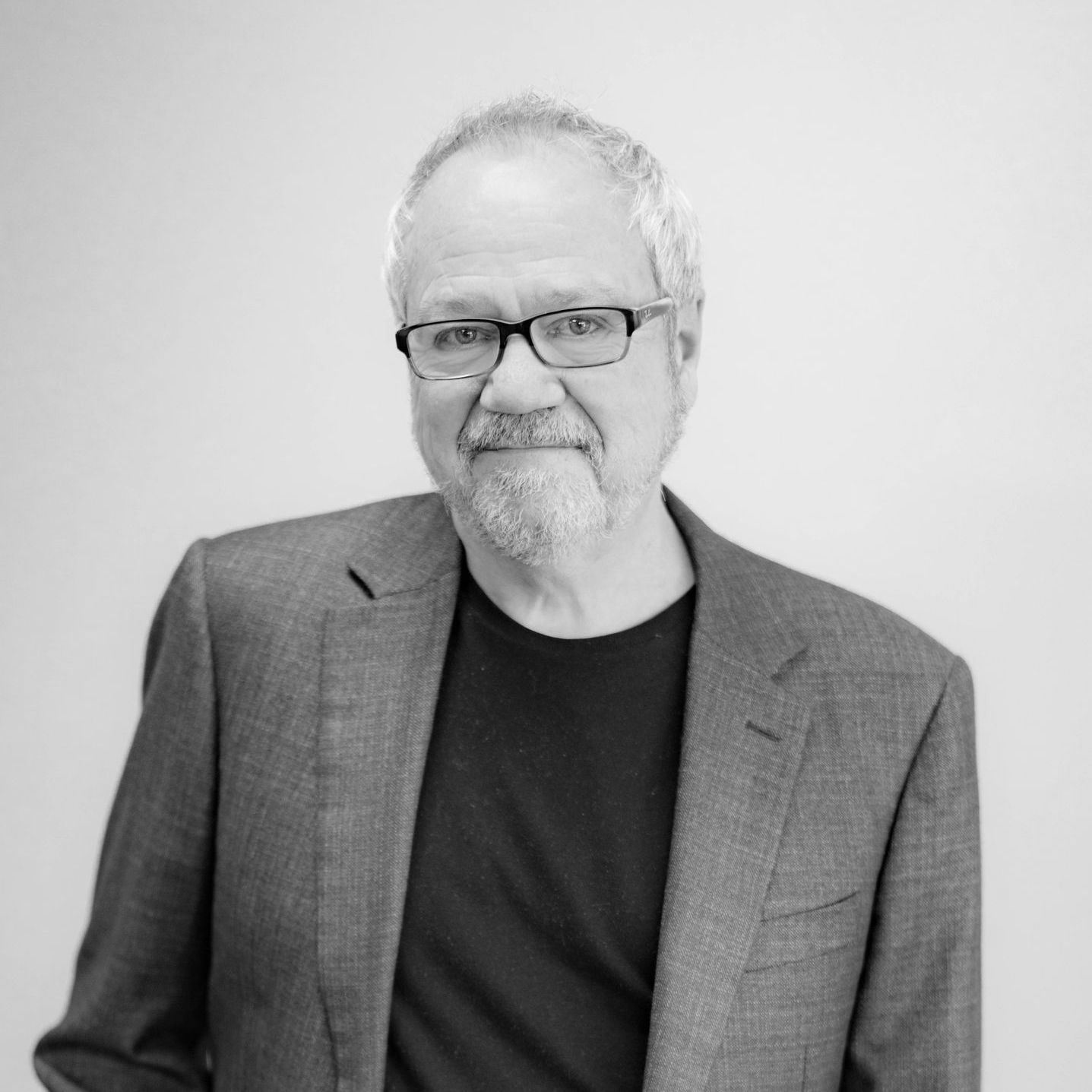 A man in a suit and glasses is standing in front of a white wall.