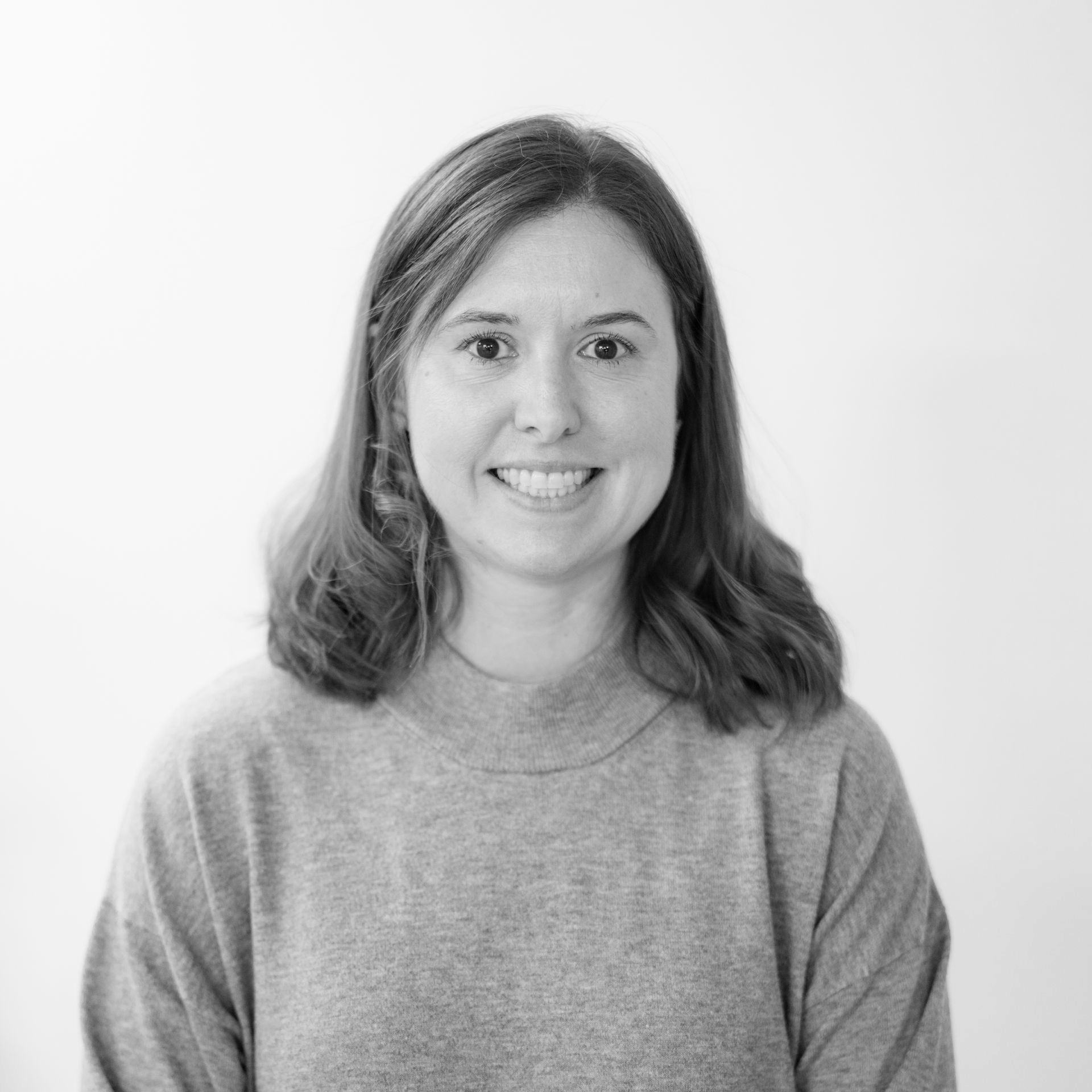 Smiling woman with shoulder-length hair wearing a gray sweater against a plain light background