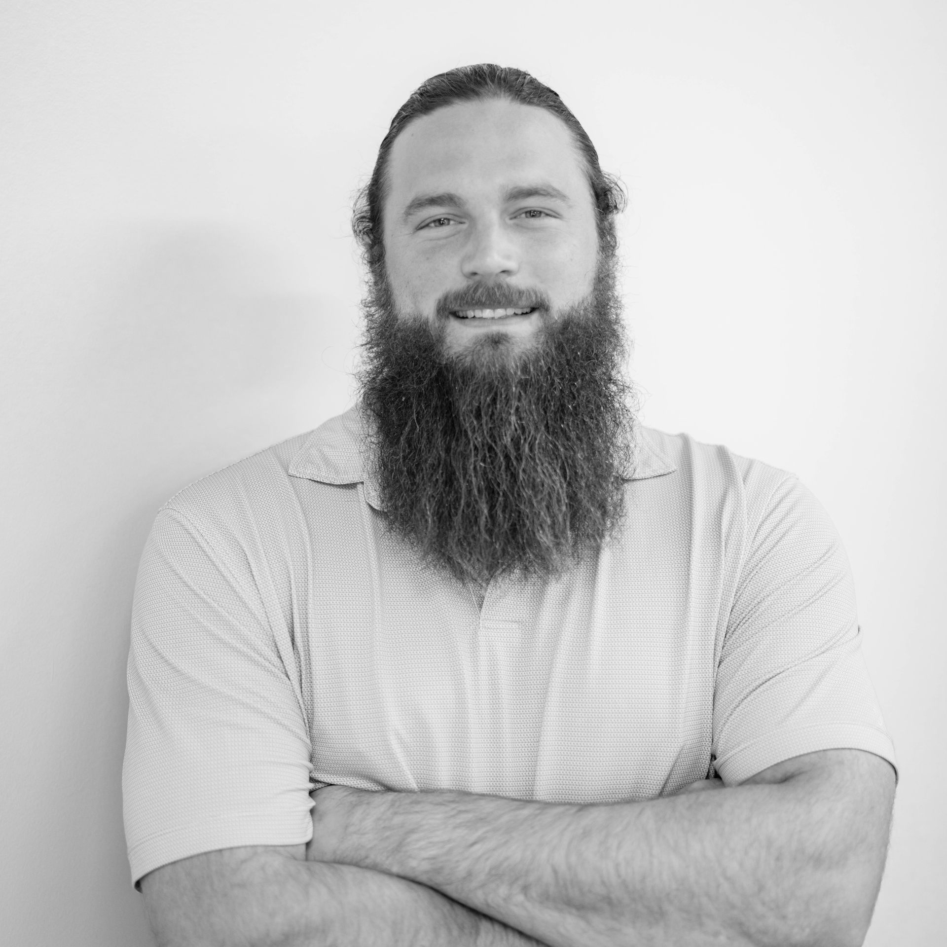 Portrait of a bearded man with arms crossed, smiling against a plain light background.