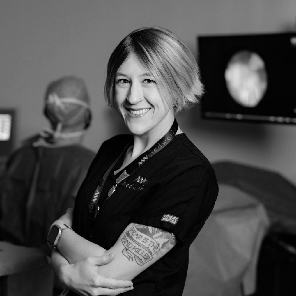 A woman with a tattoo on her arm is smiling in a black and white photo.