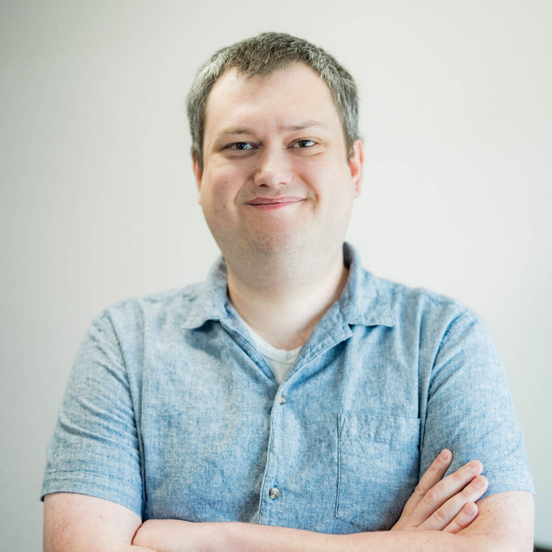 A man in a blue shirt is smiling with his arms crossed
