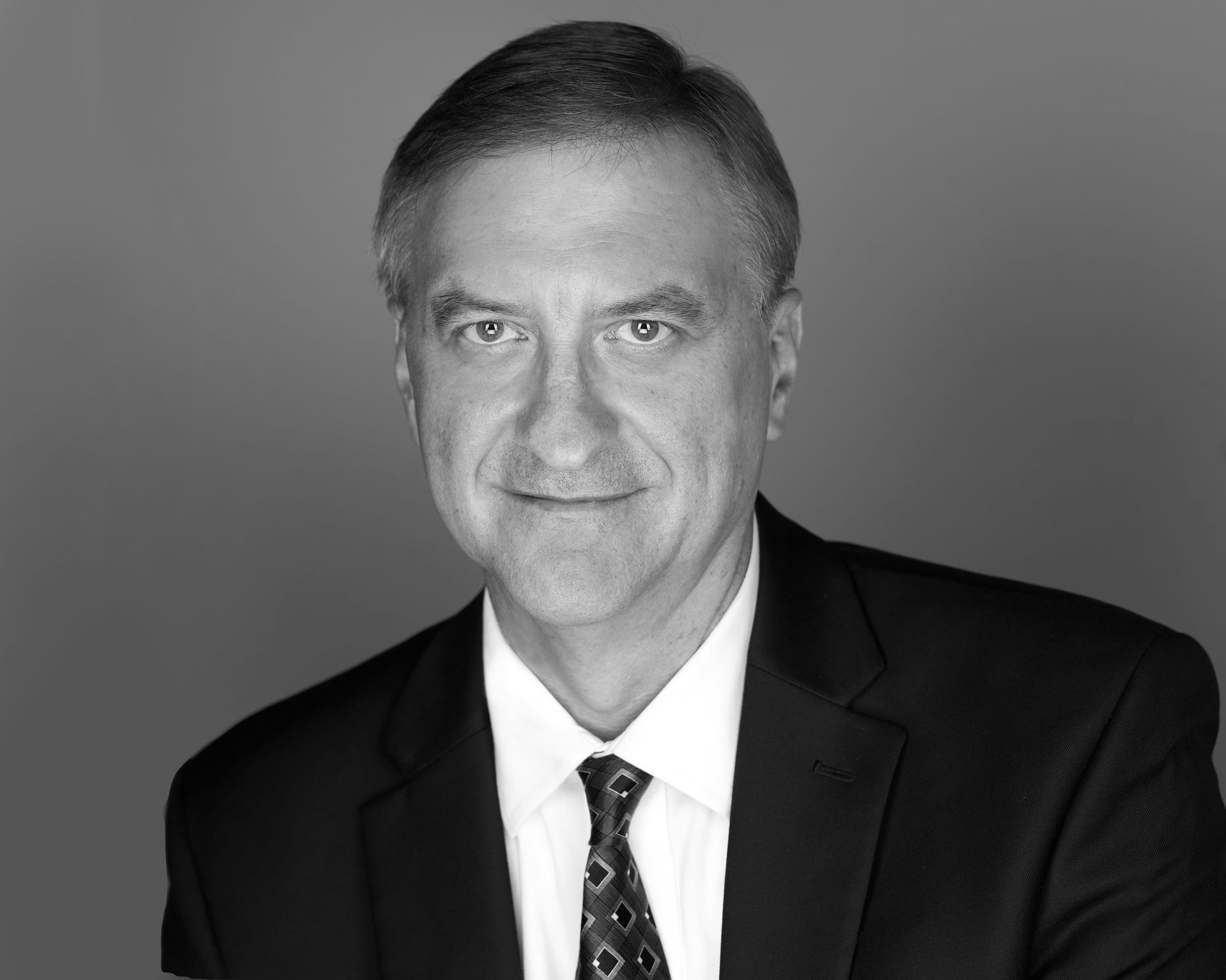 A man in a suit and tie is smiling in a black and white photo.