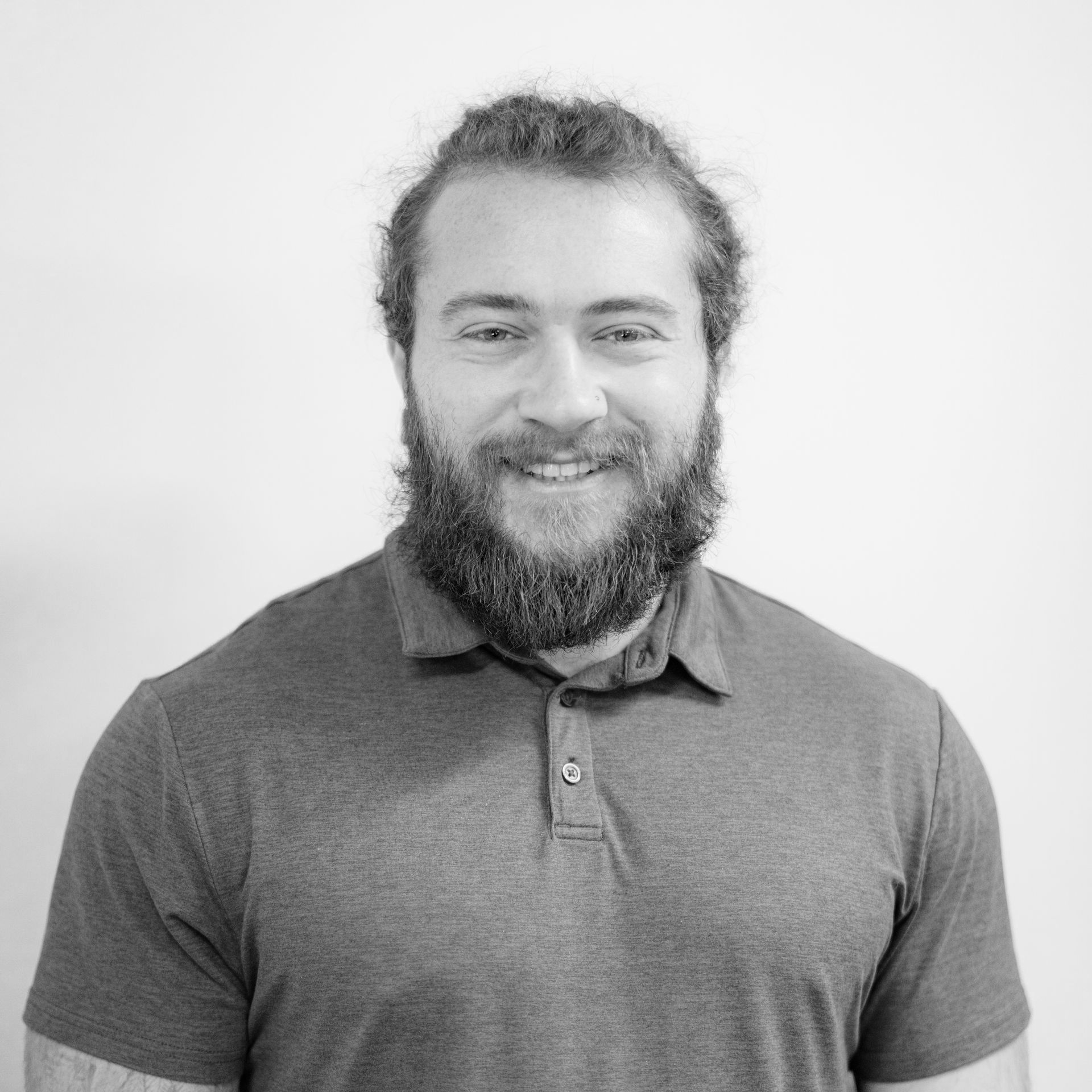 Smiling bearded man in a gray polo shirt against a plain light background